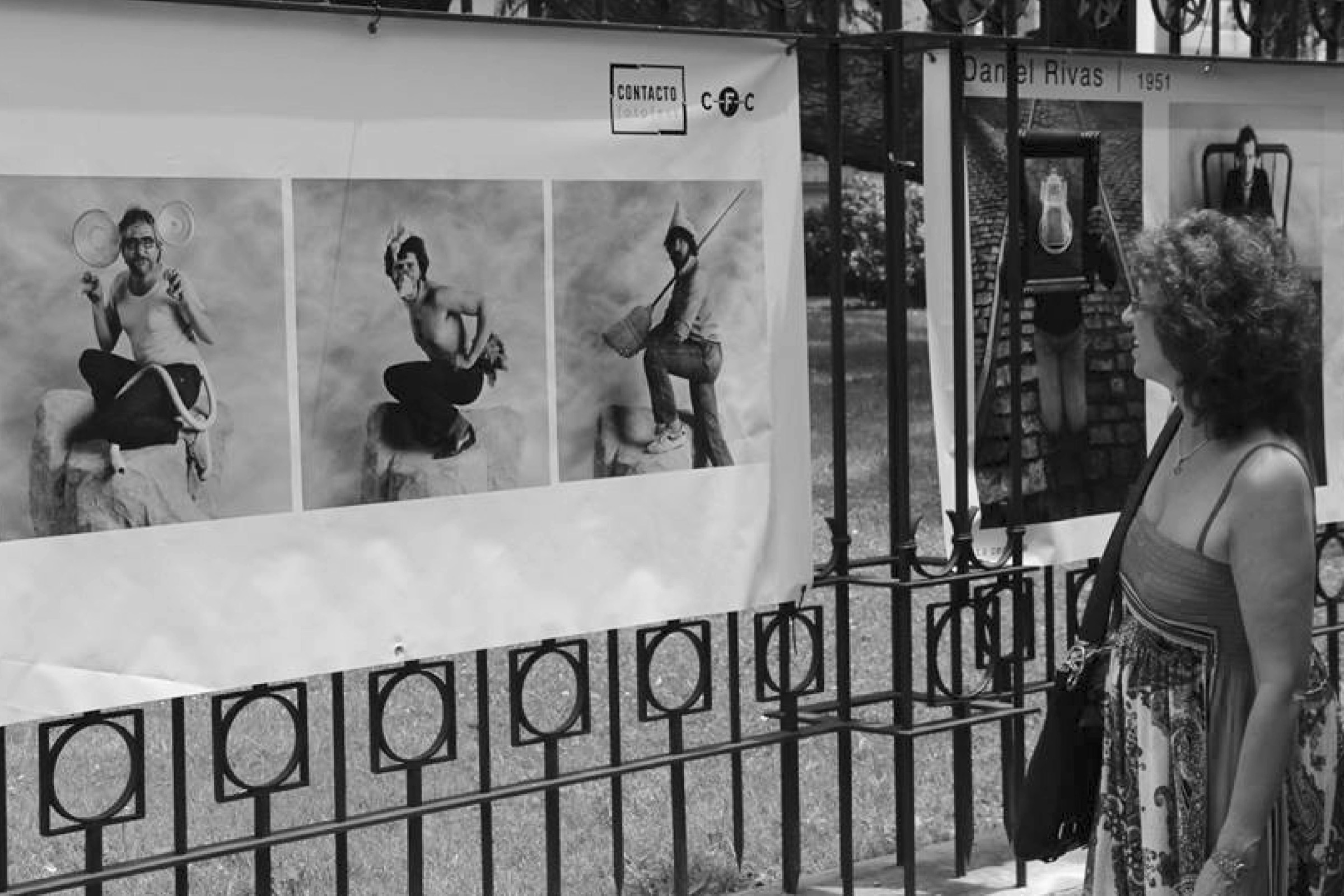 Una mujer mira una muestra fotográfica montada sobre las rejas de una casa